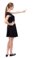 Fototapeta premium Back view of pointing woman. beautiful girl. Rear view people collection. backside view of person. Isolated over white background. Blonde in a short black dress pointing her finger.