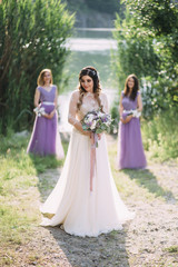 Obraz na płótnie Canvas Beautiful young lady in a delightful white dress. The bride and her bridesmaids. Wedding photography in nature, near a river. Lavender wedding colors 