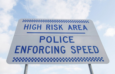 Fototapeta premium blue and white 'police enforcing speed', 'high risk area' sign and blue cloudy sky