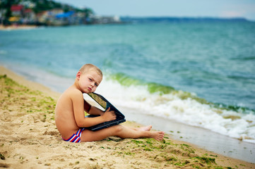 boy sitting with a laptop on the beach