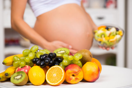 Close-up of a pregnant belly with fresh fruit and plate of salad. Healthy pregnancy, diet and vitamins