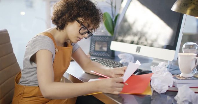  Young woman working at desk in home office with crumpled pieces of paper