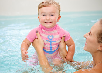 Fototapeta na wymiar Group portrait of white Caucasian mother and baby daughter playing in water diving in swimming pool inside, looking in camera, training to swim, healthy active lifestyle