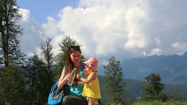 ittle girl is drinking water from a bottle in the park. Family walk in the woods. Trips to nature. Mother and daughter walking in the mountains Fresh and healthy air in the coniferous forest.