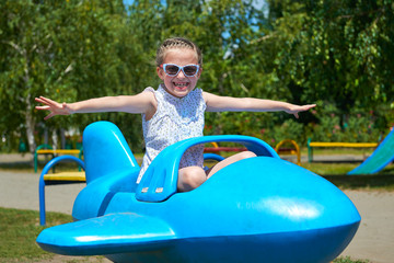 child girl fly on blue plane attraction in city park, happy childhood, summer vacation concept