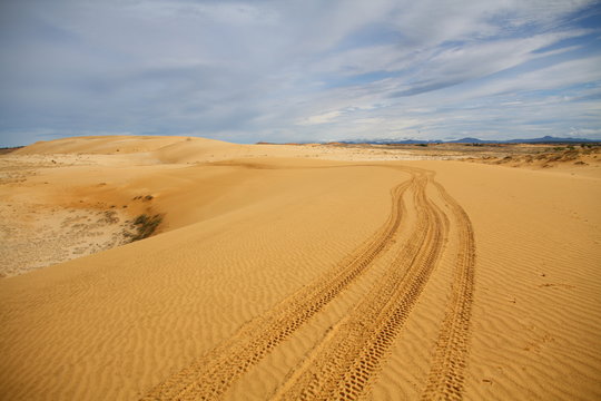 Sand dune with wheels track and cloudy blue sky
