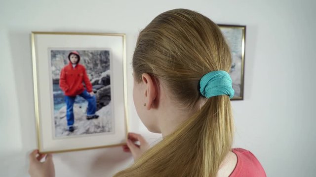 Rear view of teenage girl looks at the family framed photo prints hanging on the wall