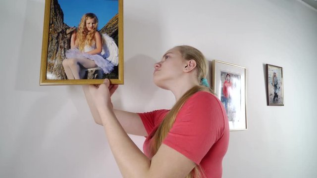 Teenage girl hanging family framed photos on wall at home