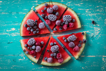 colorful tropical fruit watermelon pizza topped with berries cut into segments on a rustic wooden...