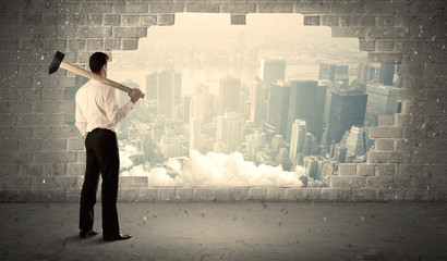 Business man hitting wall with hammer on city view
