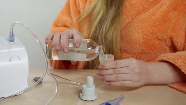 Young girl preparing to use a jet pneumatic nebulizer with breathing mask at home placing medication into the nebulizer cup for asthma or respiratory infection and pulmonary disorder treatment