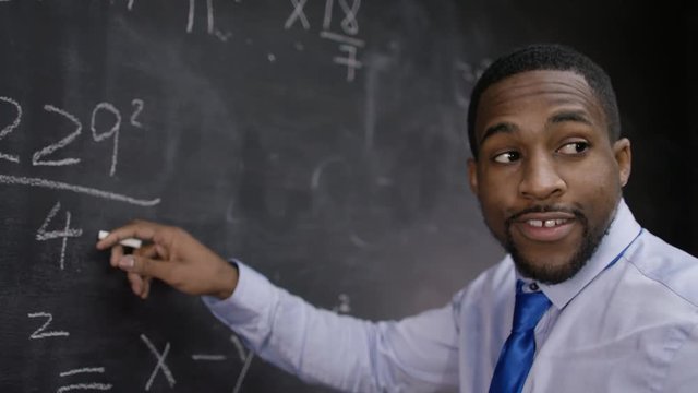  Young smiling teacher writing math formulas on blackboard
