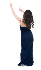 Back view of  pointing woman. beautiful girl. Rear view people collection.  backside view of person.  Isolated over white background. The dark curly girl in blue evening dress shows both hands up.