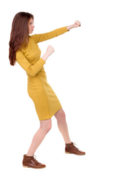 skinny woman funny fights waving his arms and legs. Isolated over white background. Long-haired brunette in a mustard-colored dress hands fights.
