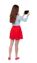 Naklejka premium back view of standing young beautiful woman using a mobile phone. girl watching. Rear view people collection. backside view of person. Isolated over white background. Long-haired brunette in red