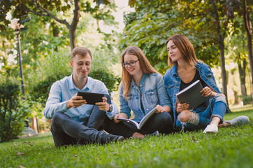 happy students sit on the grass in the park study materials and 