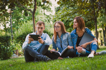 Naklejka premium happy students sit on the grass in the park study materials and 