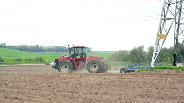 An agricultural tractor plowing a field. Hills and a forest at the background.