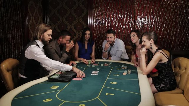 The company of players at the poker table place their bets.