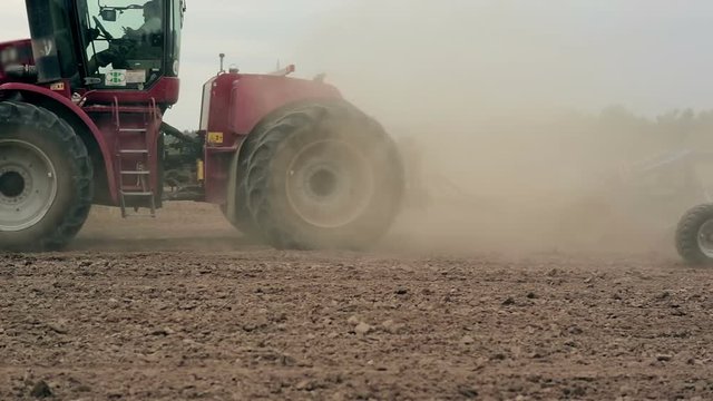 A side view of an agricultural tractor, plowing a field, soil dust. close-up