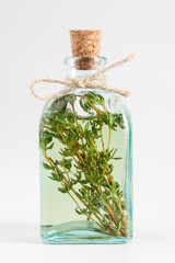 Transparent bottle of thyme essential oil or infusion on white.