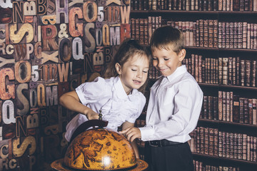 Children boy and girl of school age consider a globe