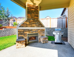 Cozy covered patio interior with stone trim fireplace and barbecue.
