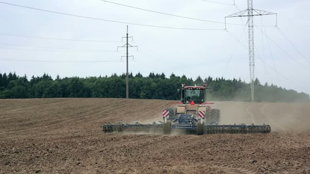 An agricultural tractor, plowing a field before sowing, moving from the camera. A forest in the background.