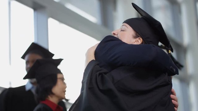  Happy group of mature students on graduation day, man congratulates his wife 