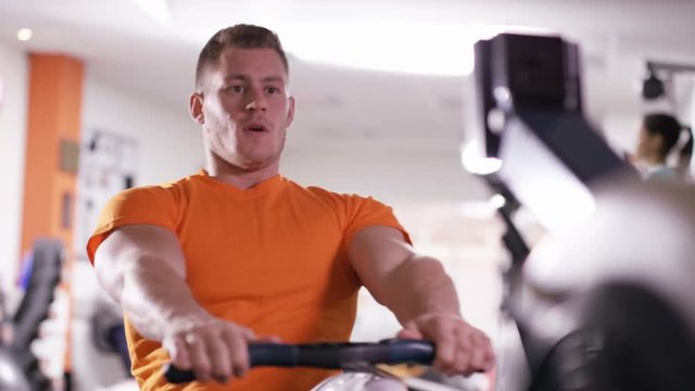  Muscular man with prosthetic leg working out on rowing machine at the gym