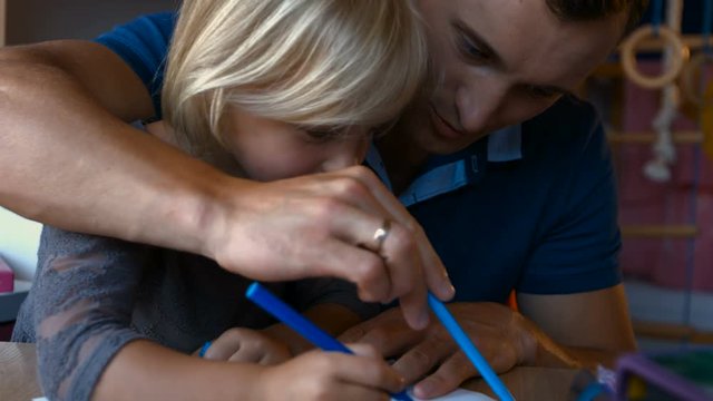 Adorable kid with long blond hair and his dad drawing with color pencils, close-up
