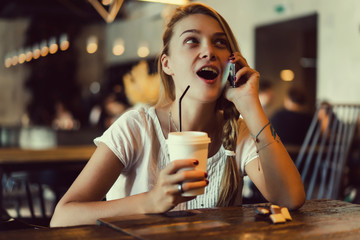 Young pretty woman using smartphone in cafe, drink coffee in cup, sweet breakfast, happy face, outdoor hipster portrait, fashion girl, table, sweet drink, tasty tea, aromatic coffee