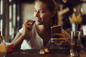 Young pretty woman using smartphone in cafe, drink coffee in cup, sweet breakfast, happy face, outdoor hipster portrait, fashion girl, table, sweet drink, tasty tea, aromatic coffee