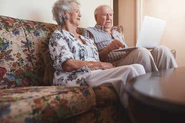 Elderly couple relaxing on sofa and using laptop