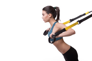 Upper body excercise concept. Beautiful woman exercising with suspension straps alone in studio....