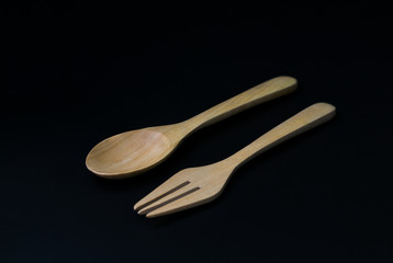 Handcrafted wooden kitchen utensils with a fork and spoon isolated on black background