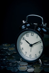 saving time, Alarm clock standing with coins isolated on black background. with vintage filter