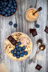 Gluten free amaranth and quinoa porridge breakfast bowl with blueberries and chocolate over rustic wooden background. Top view, overhead, flat lay. Copy space
