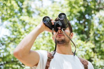 Man with backpack looking through binoculars in forest