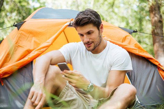 Man tourist using mobile phone in toristic tent at forest