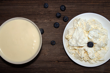 Cottage cheese, sour cream and bilberry on old wooden table.