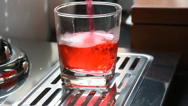 Human hand pour sweet red drink from cooler machines on counters into glass