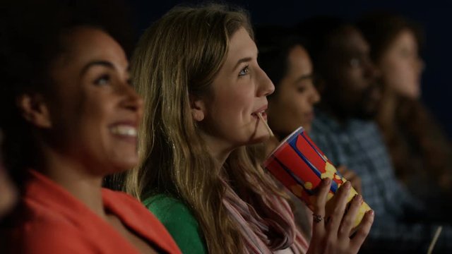 Happy young female friends watching a film in movie theatre