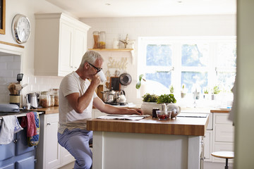 Middle aged Caucasian man sits in kitchen reading newspaper