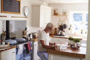 Middle aged Caucasian man sits in kitchen reading newspaper