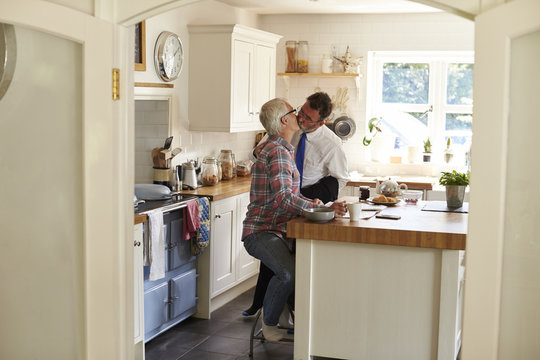 Gay men kissing in kitchen before work, full length