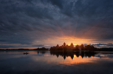 Fototapeta na wymiar Fantastically beautiful summer sunrise over Trakai Castle in Lithuania,the fisherman in the boat and the sun's rays over the castle