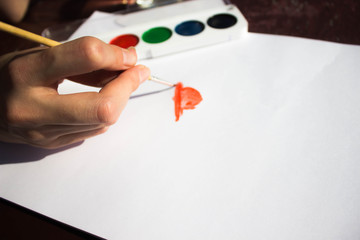Рука художника рисует красками и акварелью на белом листе бумаги женщину с шляпкой сумочкой и в платье