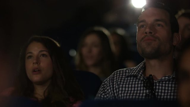 Man laughing loudly in cinema audience making his girlfriend embarrassed