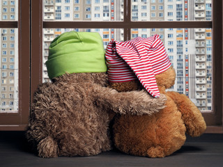 Two friends looking out the window at the windows of the house. Toys colorful hats bear cubs. Embrace the . Concept - love, friendship, support, dreams  a new home, apartment